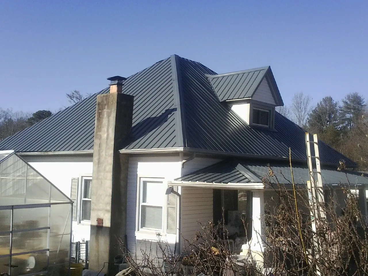 Dark blue standing seam metal roof on a white farmhouse with dormer — Slate & Tile Roof Repair by Roofing Brothers in Gardiner