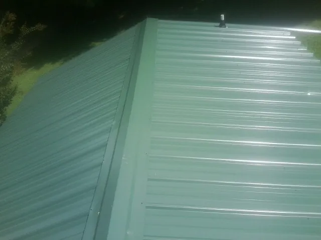New green metal panels meeting at the ridge of a roof — Flat Roof Repair work by our crew in Gardiner