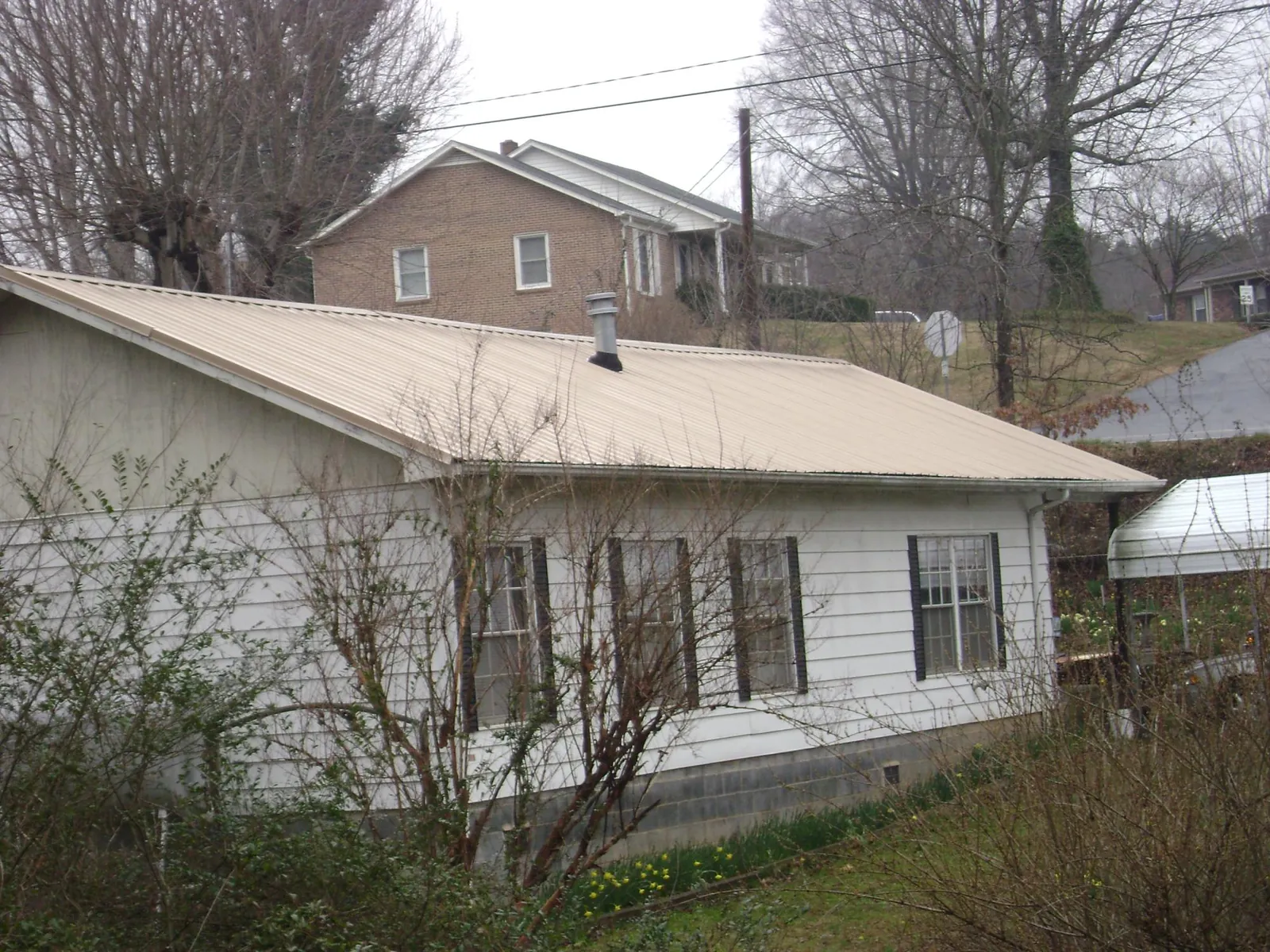 Tan metal roof on a white sided house set into a hillside — Commercial Roofing by Roofing Brothers in Gardiner